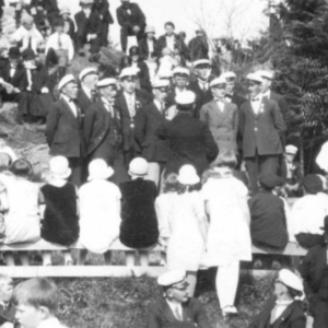 12 menn i dress og skipperlue som synger ved utendørs høytidstilstening. Haugesund, ca 1920. Arkivkode MHB-F.000590.